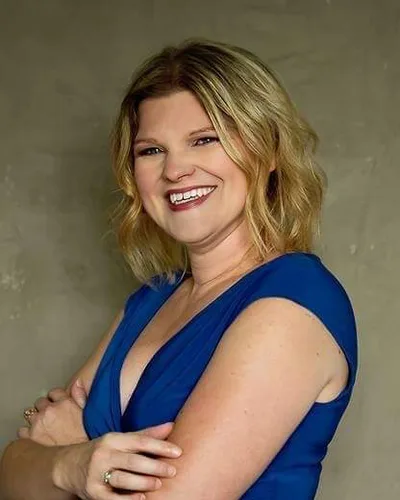 Amy Herdine, licensed agent at Tierra Vista Health, smiling with arms crossed in a blue top against a gray backdrop